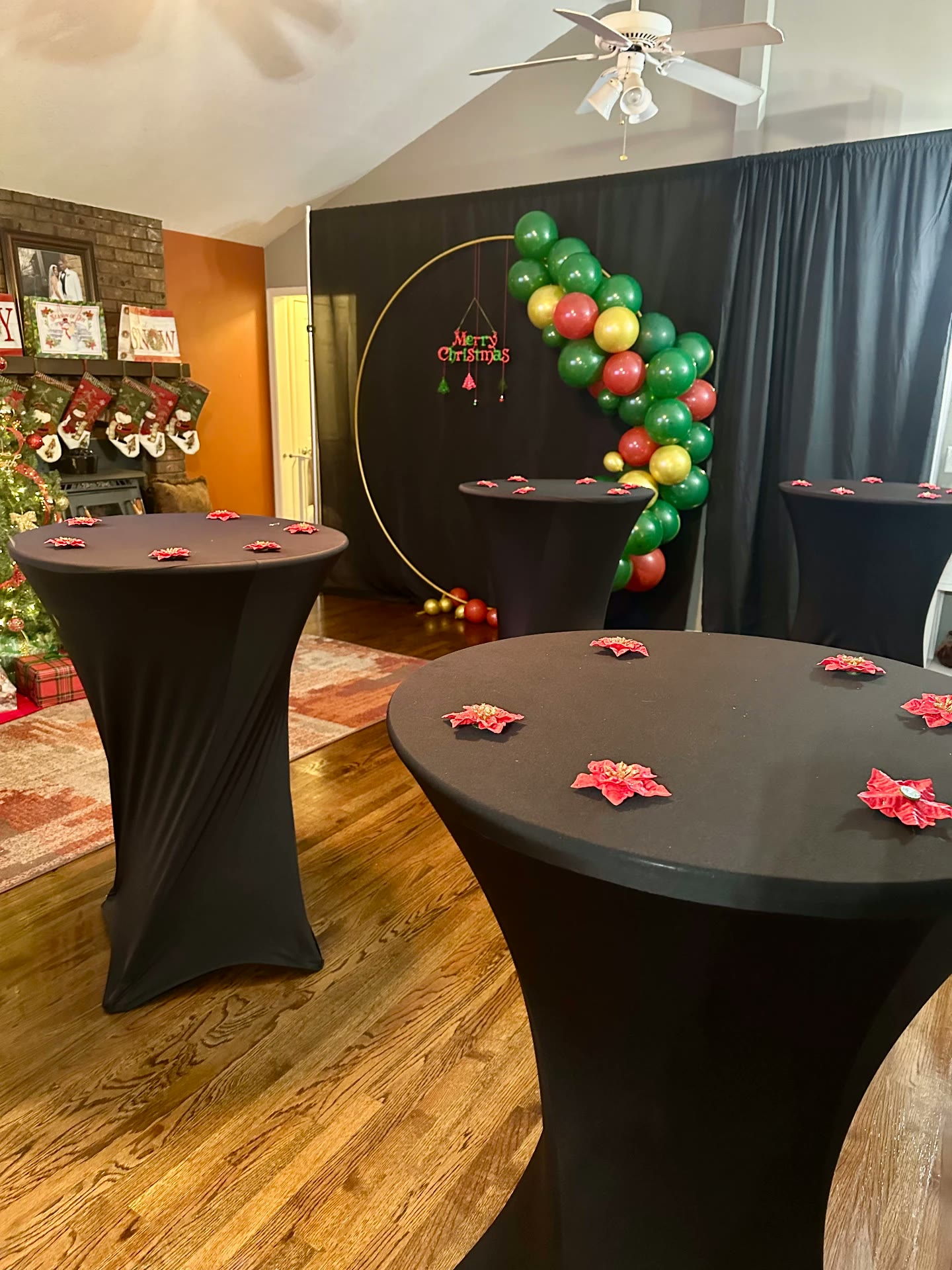 Holiday party setup with black cocktail tables and a red, green and gold balloon arch